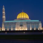 A Panorama of the Sultan Qaboos Grand Mosque in Muscat, Oman in the early evening hour showing off the dark blue sky and glowing